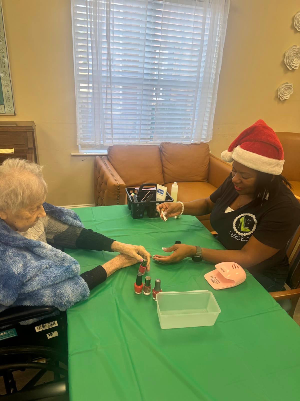 LIPSC volunteer in a Santa hat polishing a senior's nails during a holiday visit